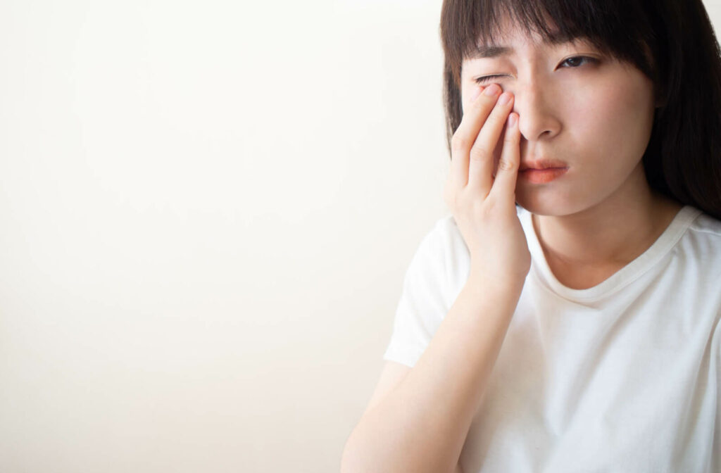 A young woman rubbing her irritated right eye with dry eyes.