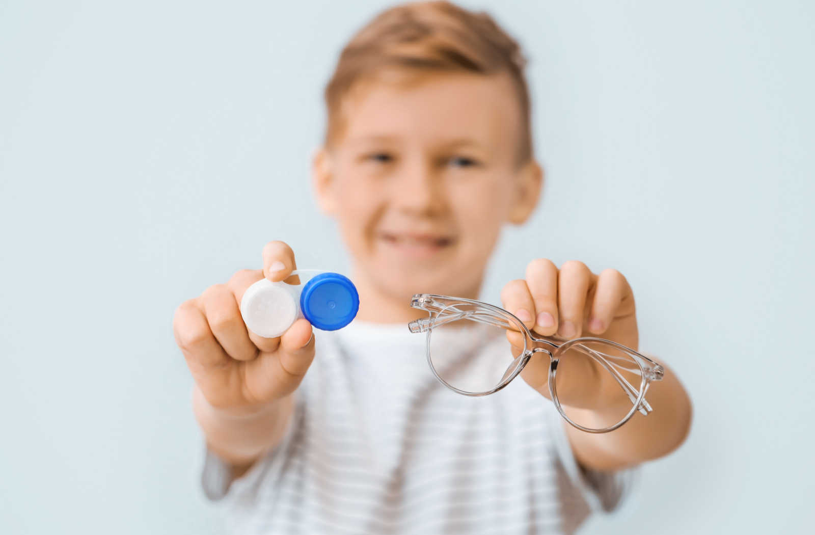 A little boy is holding and showing eyeglasses with corrective lenses and specially designed contact lenses for his myopia