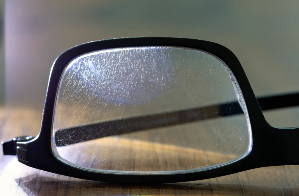 A close-up of eyeglasses with a lens covered in scratches.