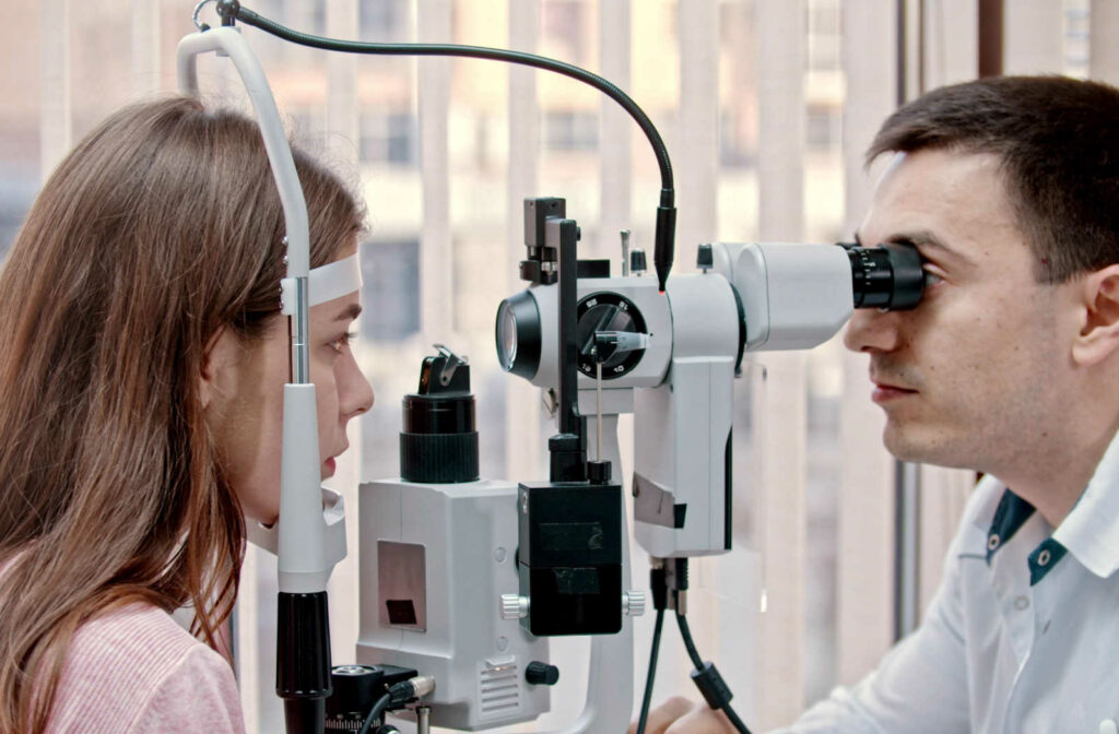 A male Ophthalmologist is examining a  young woman's retina with a used of a slit lamp.
