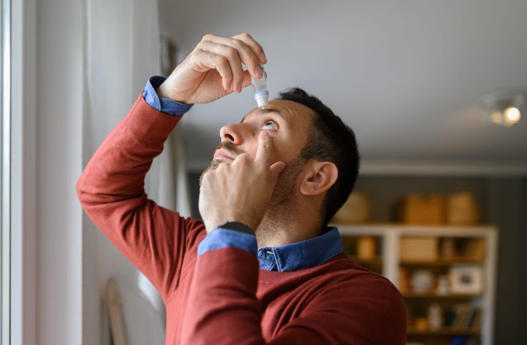 A young man applying eye drops to his dry eyes.