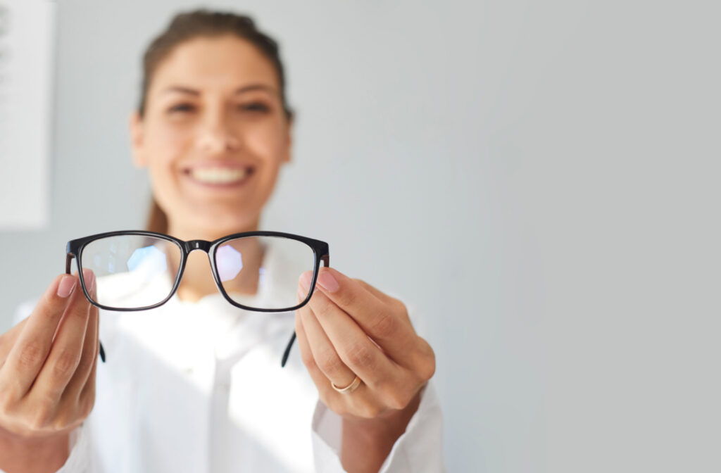 An optometrist holding a pair of eyeglasses while smiling at the camera