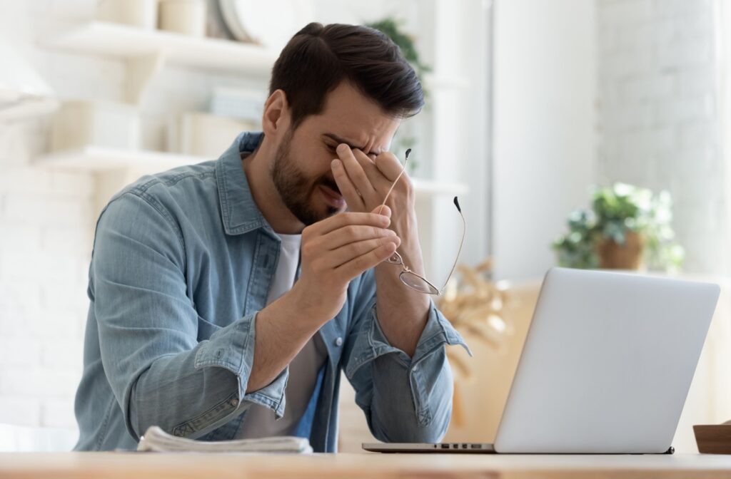 A young man working at his computer with his glasses off rubbing his eyes due to dry eye discomfort.