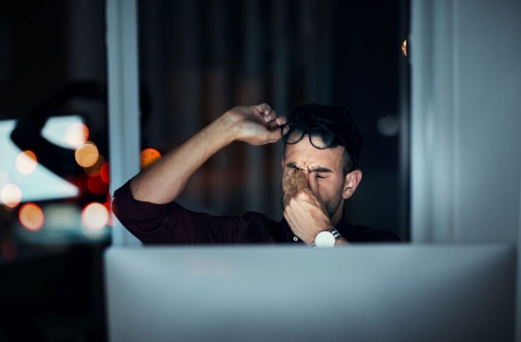 An office worker working at a computer late into the night rubs their uncomfortable eyes.