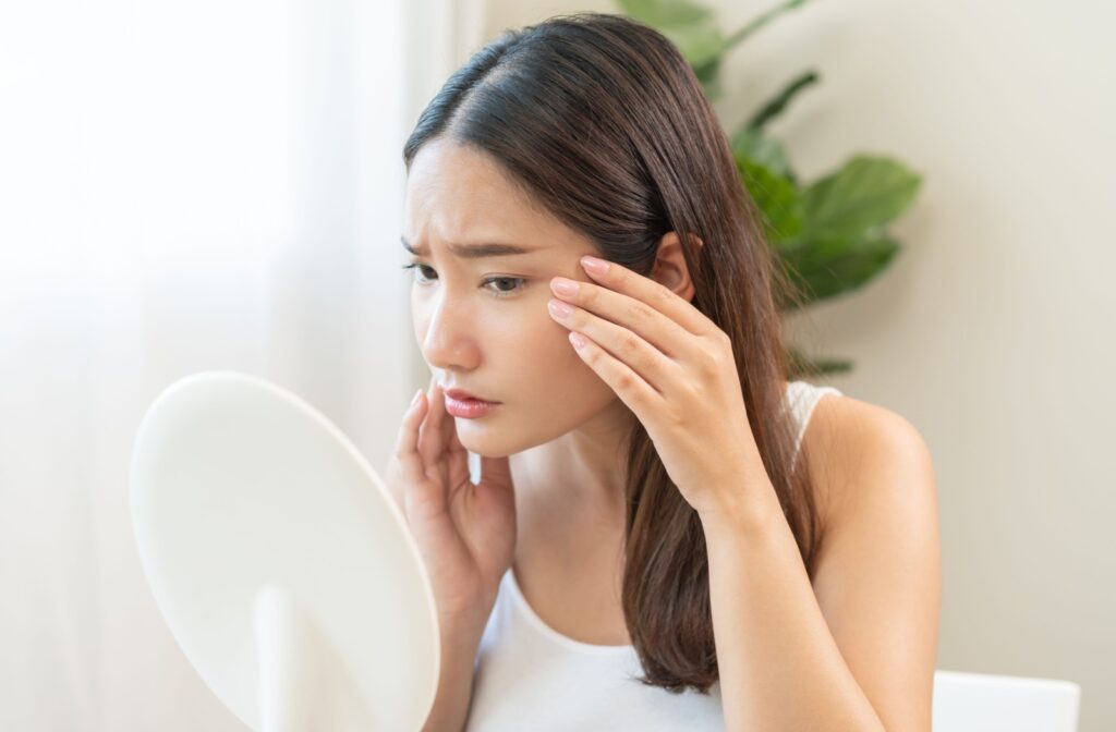 A woman looking at her reflection in the mirror with concern for the dry skin under her eyes.