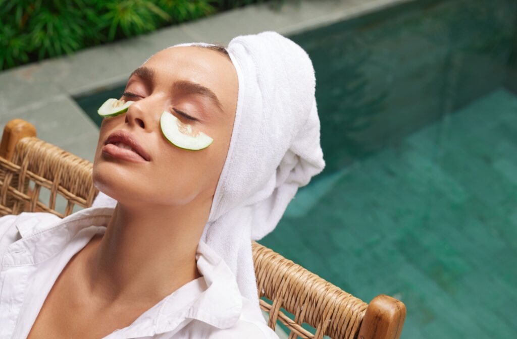 A person relaxes by a pool with cooling cucumber slices placed under their eyes to help with under-eye bags.