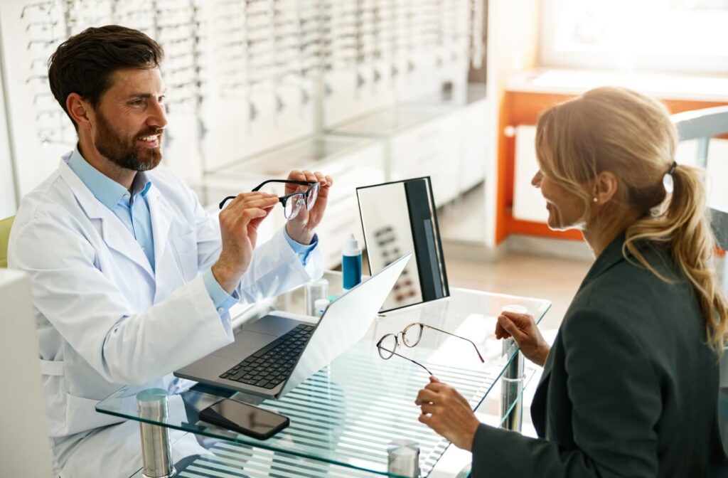 An optometrist holding a pair of eyeglasses while explaining the benefits of anti-reflective lens coating to their patient.