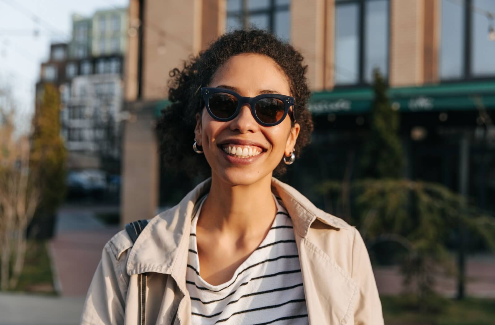 Person wearing UV-protective sunglasses and smiling outdoors.